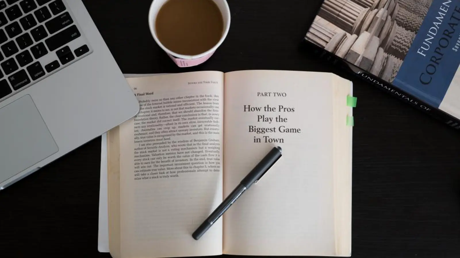 Livro aberto com caneta, notebook e café sobre uma mesa escura