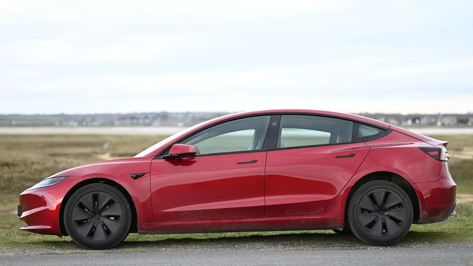 Tesla Model 3 vermelho visto de lado, parado em um campo